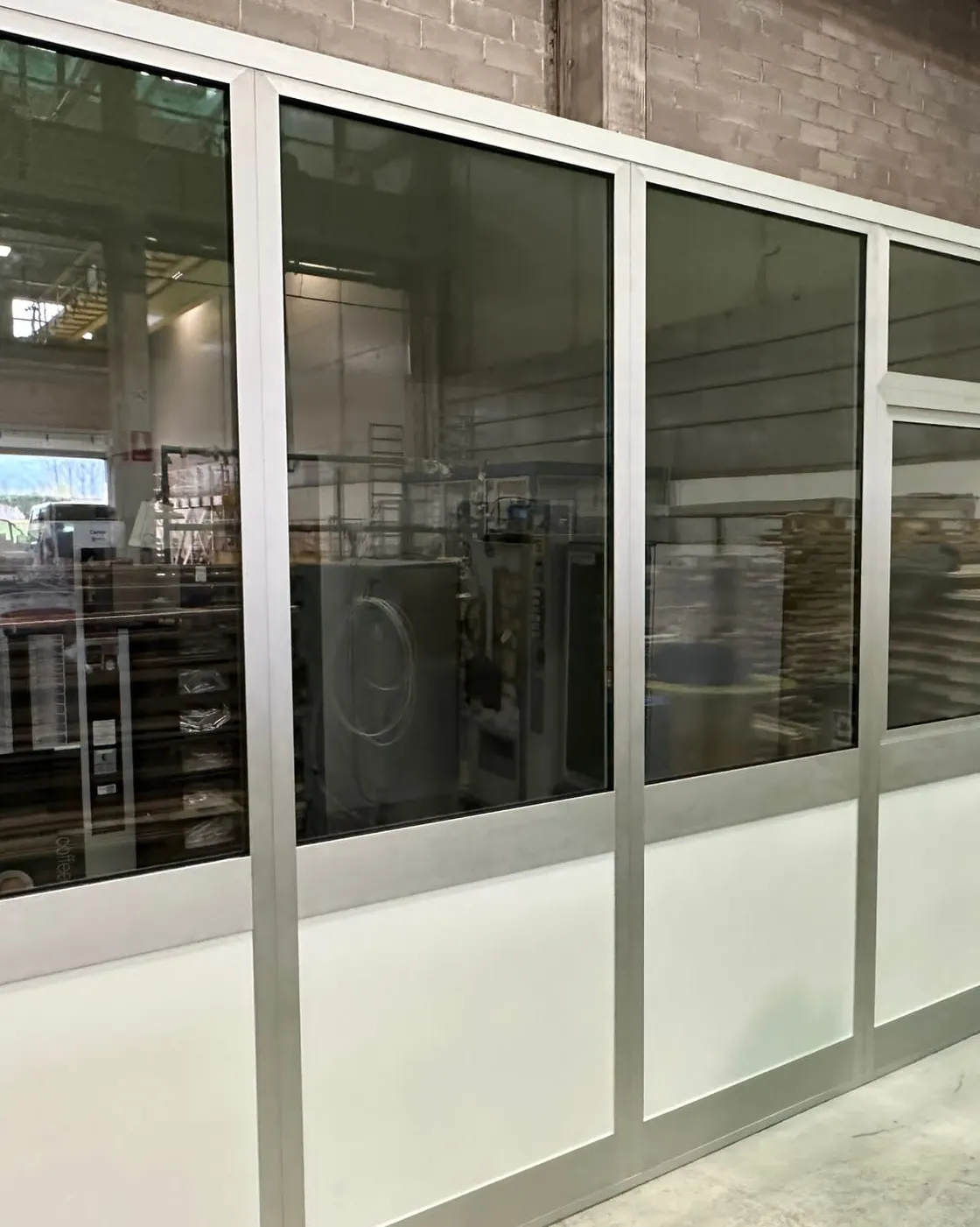 Box ufficio vetrato con zoccolo in pannello dentro un capannone