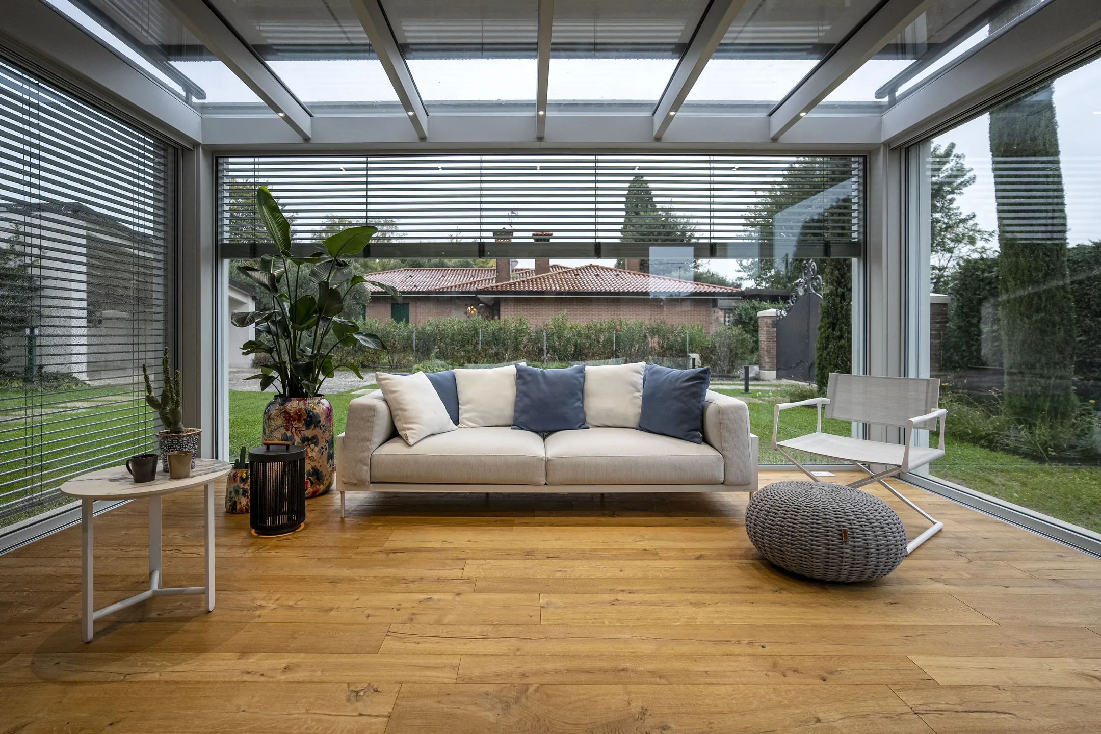 L'interno di una veranda Qubo con il tetto in vetro, il divano e il giardino oltre le vetrate